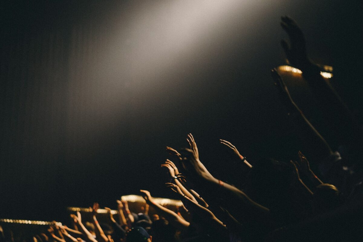 Raised hands reaching toward a beam of light in a dark worship gathering